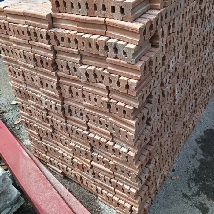 A close-up image of red clay brick, conforming to Thai Industrial Standard (TIS) 77-2565, clearly shows the pores and surface texture. It is strong and meets the standards for high-quality construction projects.