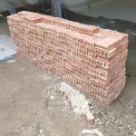 Red clay bricks are neatly arranged in long rows at the construction site, ready for building the walls.