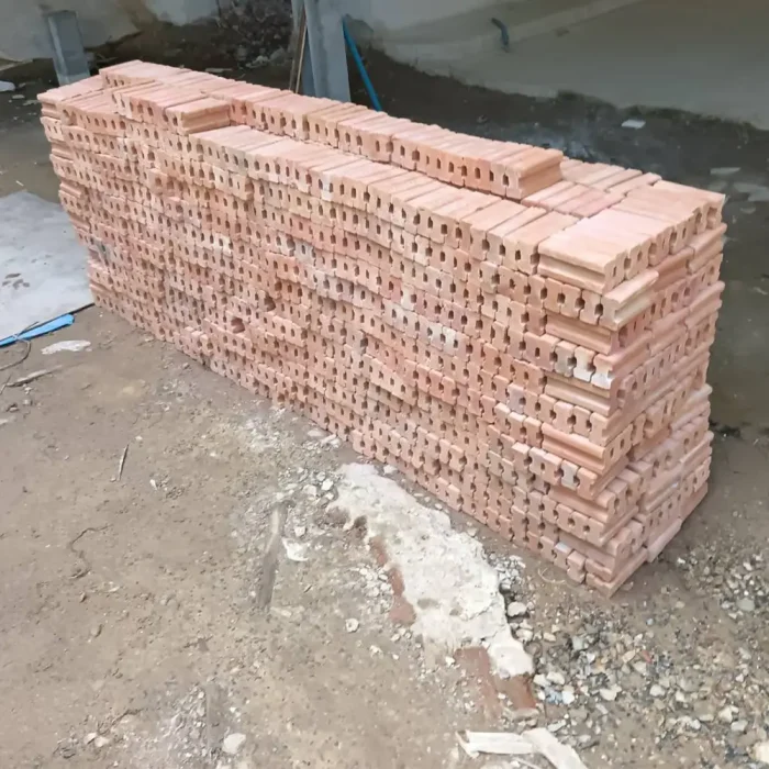 Red clay bricks are neatly arranged in long rows at the construction site, ready for building the walls.